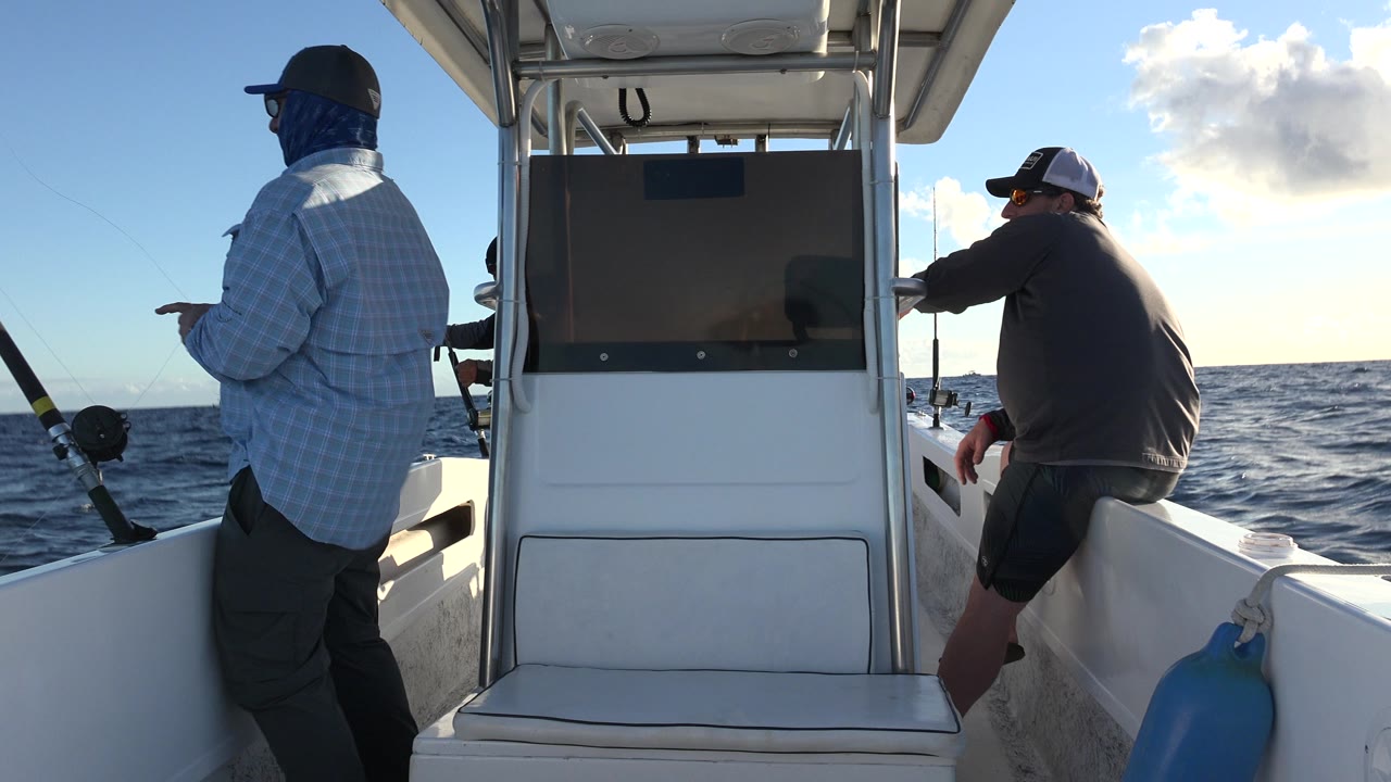Two men on a fishing boat with rods and open ocean behind them.