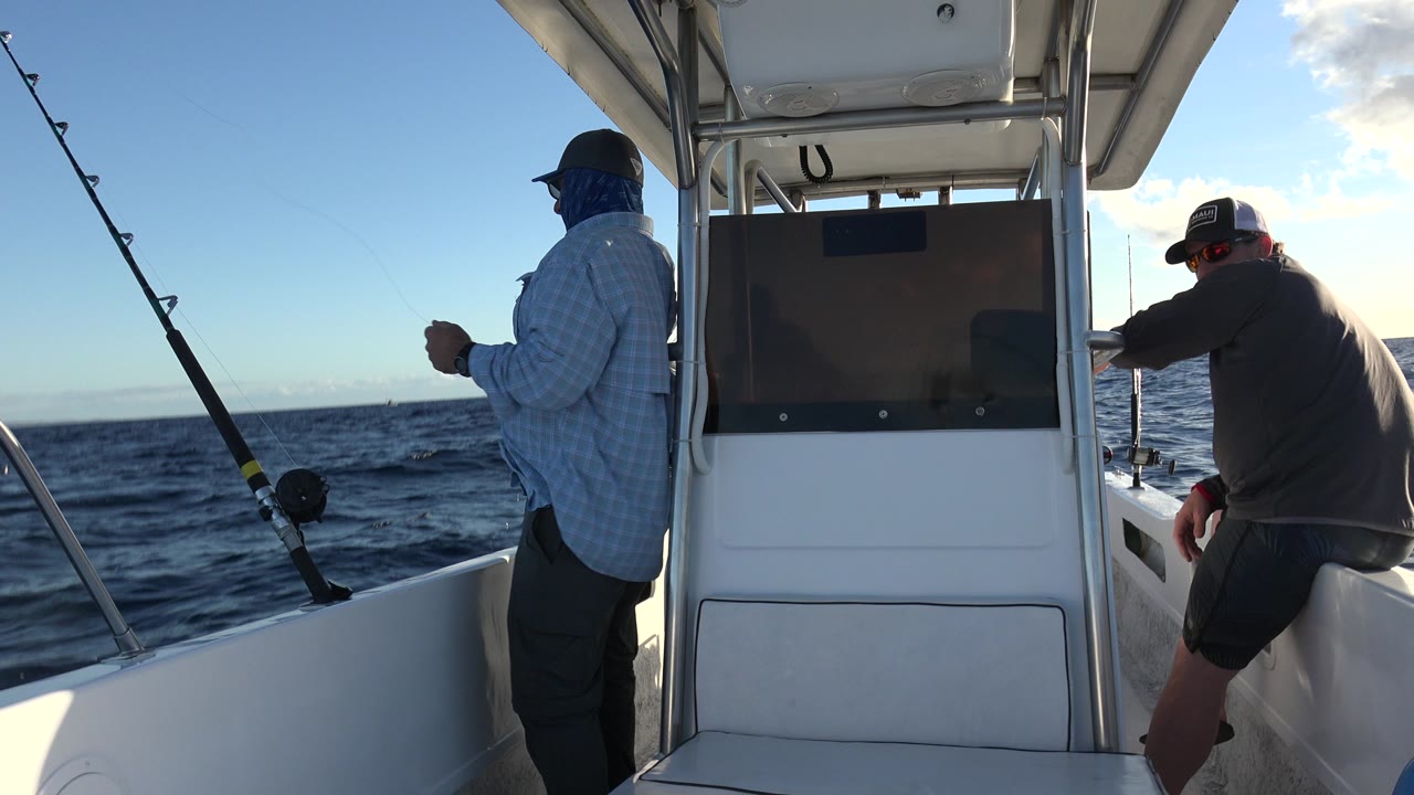 One second in, the standing angler holds his hands near his chest while another man sits on the starboard side, with fishing rods angled over the Los Cabos water.