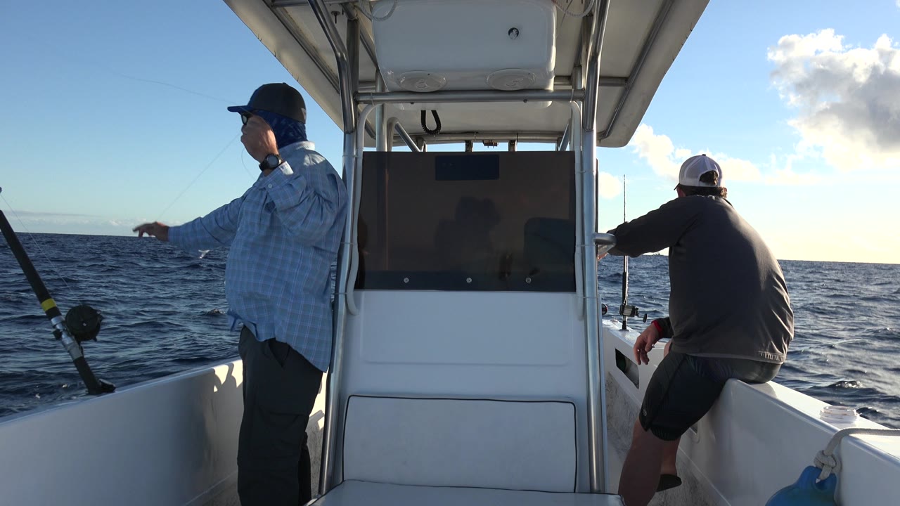 Man on boat points toward the ocean beside mounted fishing rods