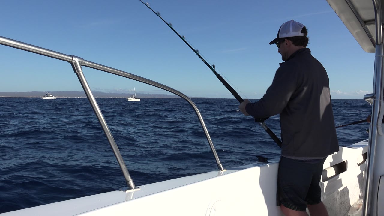 Man reels a fishing rod while standing on a small boat.
