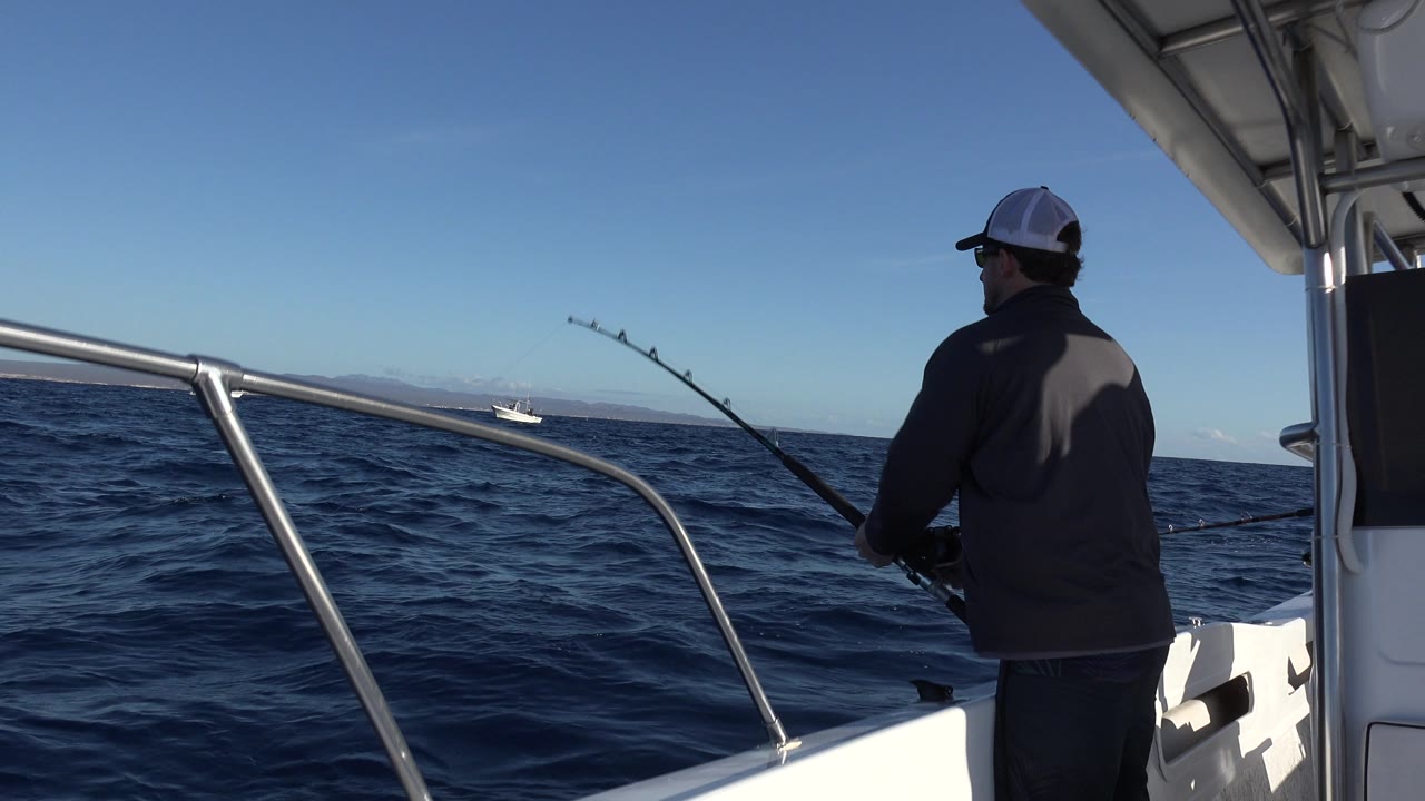 Man fishes near the starboard side of a white boat.