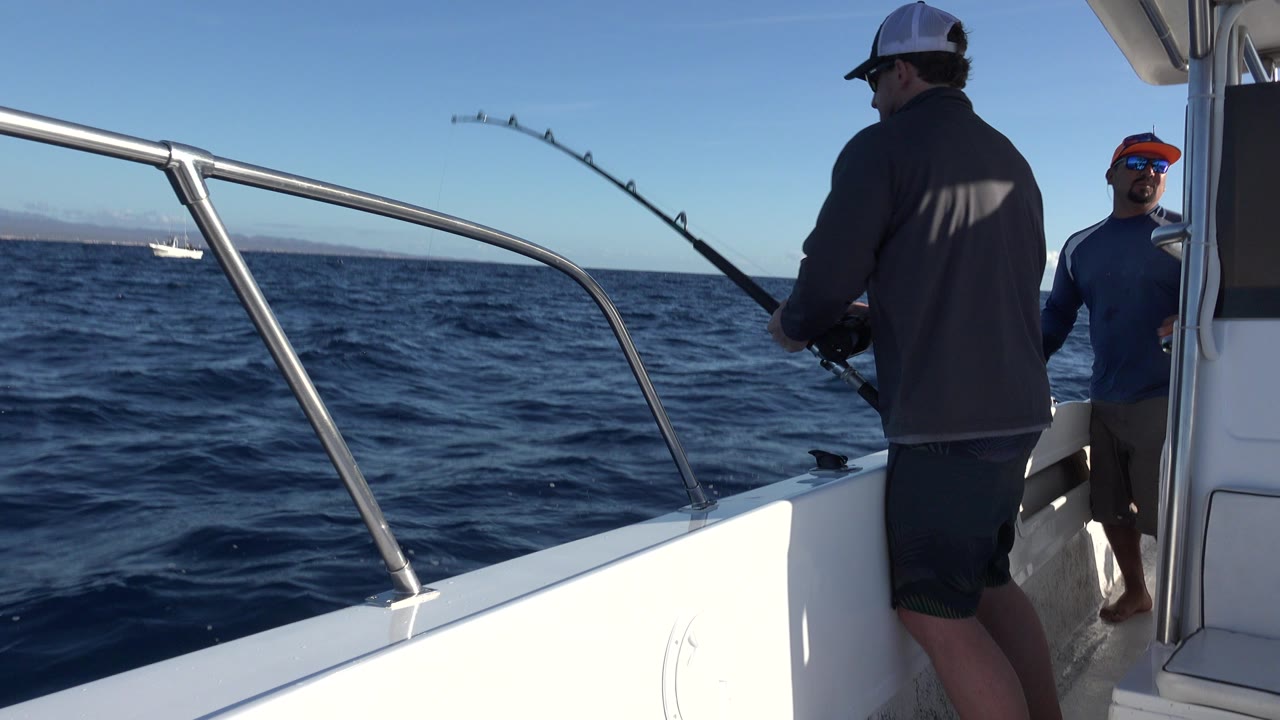 Man reeling a fishing rod from a white boat on open water.