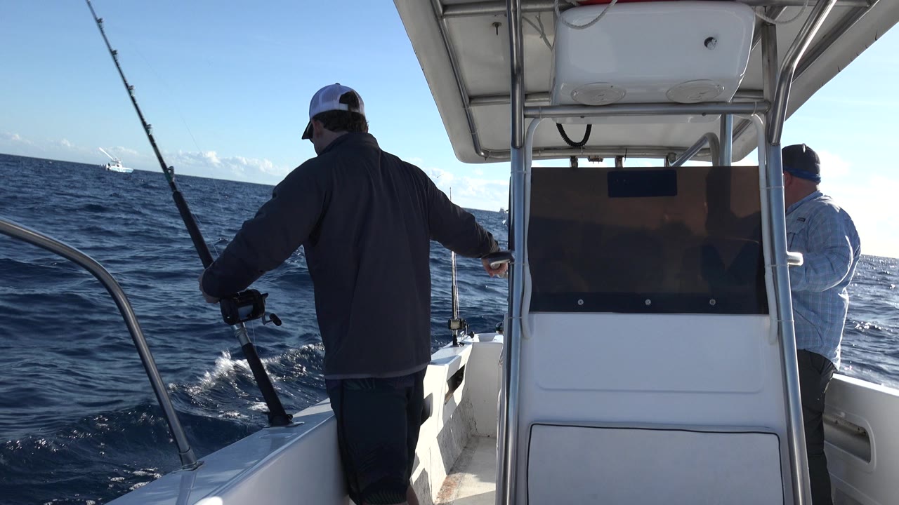 Man holding a fishing pole on a white boat at sea