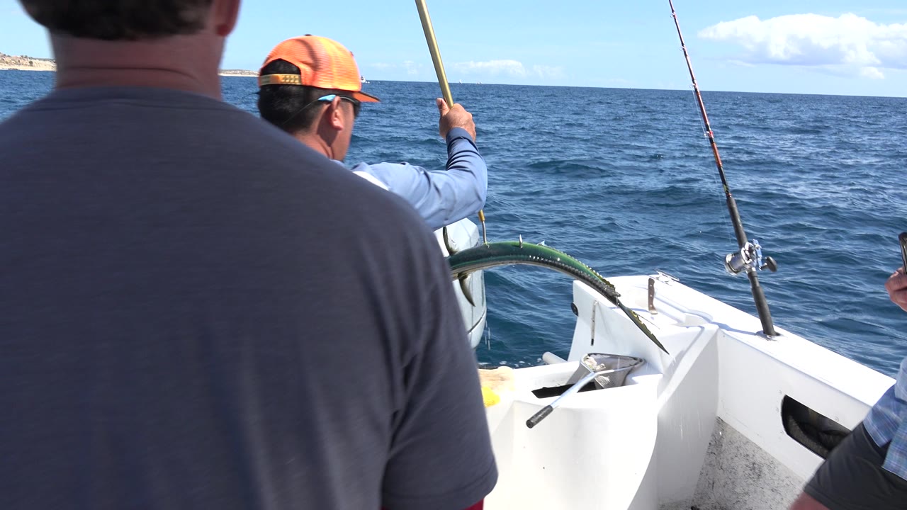 A similar Los Cabos boat-level view shows a man in a gray shirt in the foreground and a man in an orange cap holding a rod toward the open sea.