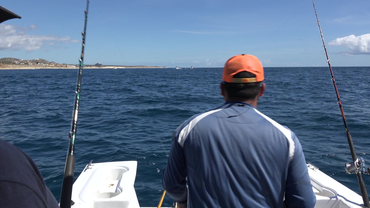 Man in orange cap facing the ocean from a fishing boat.