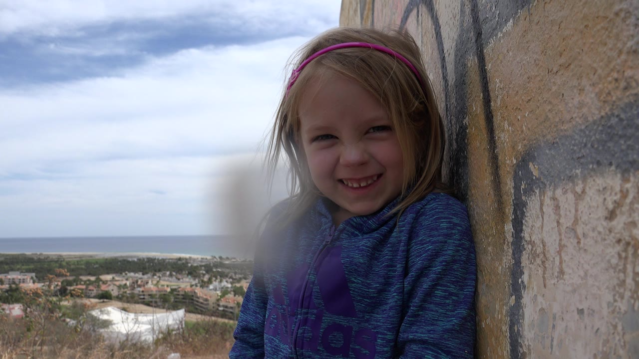 Young girl smiling beside a painted wall with coastal town and ocean behind her.