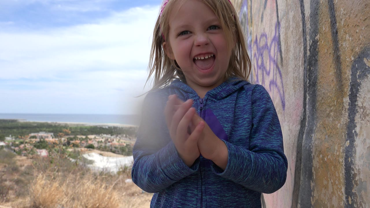 Blonde child smiling beside a marked wall on a hilltop.