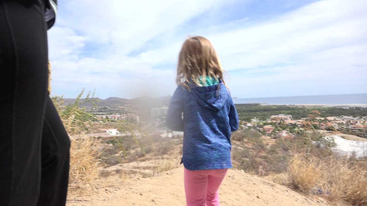 Adult woman partly in foreground and girl facing coastal view on arid slope.