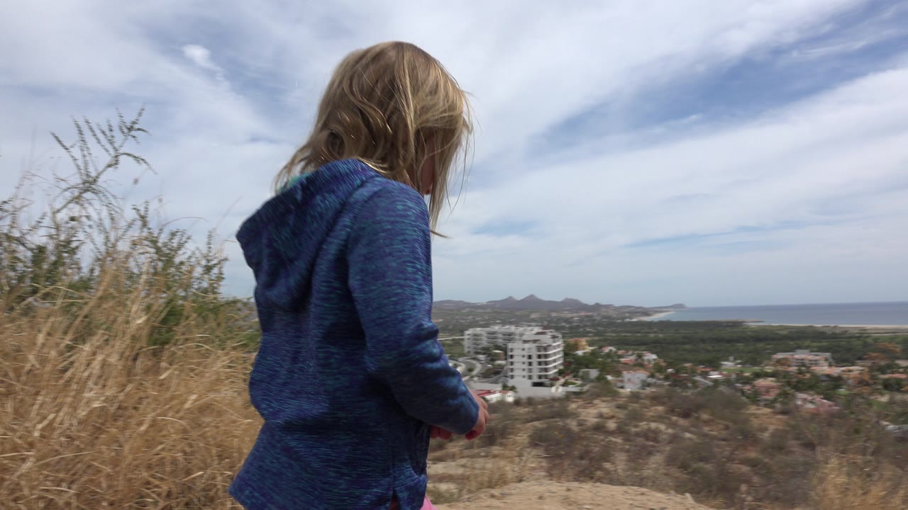 Child turns away on hill with ocean and town in background.