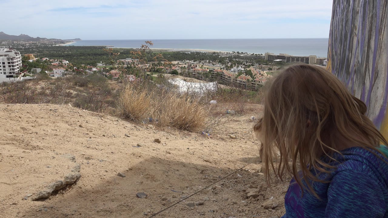 Child at right edge overlooking a sandy hillside and coast.