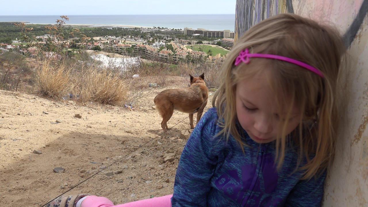 Young girl beside a wall with a small dog on a dusty hillside.