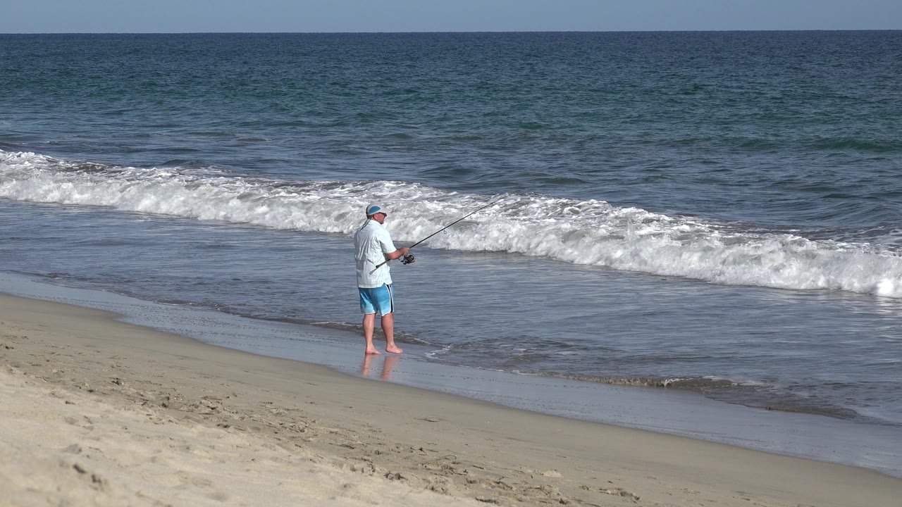 Lone fisherman on the beach facing incoming surf.