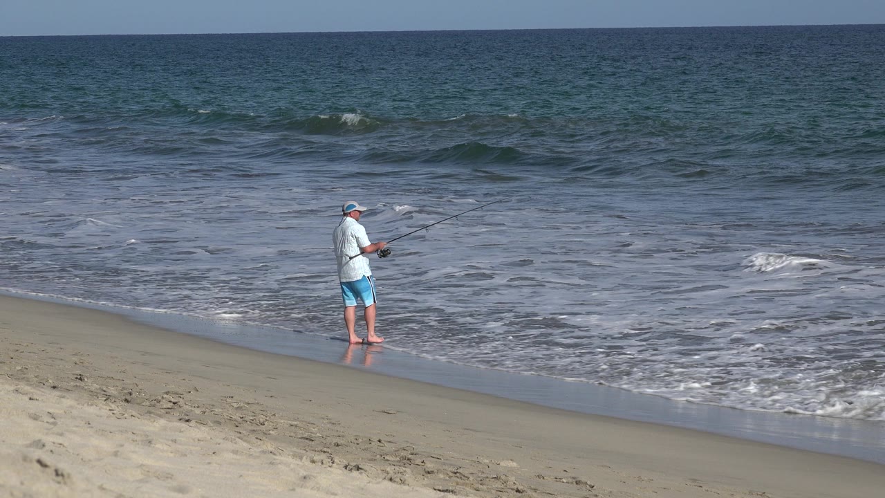 Beach fisherman facing the water with waves rolling in.