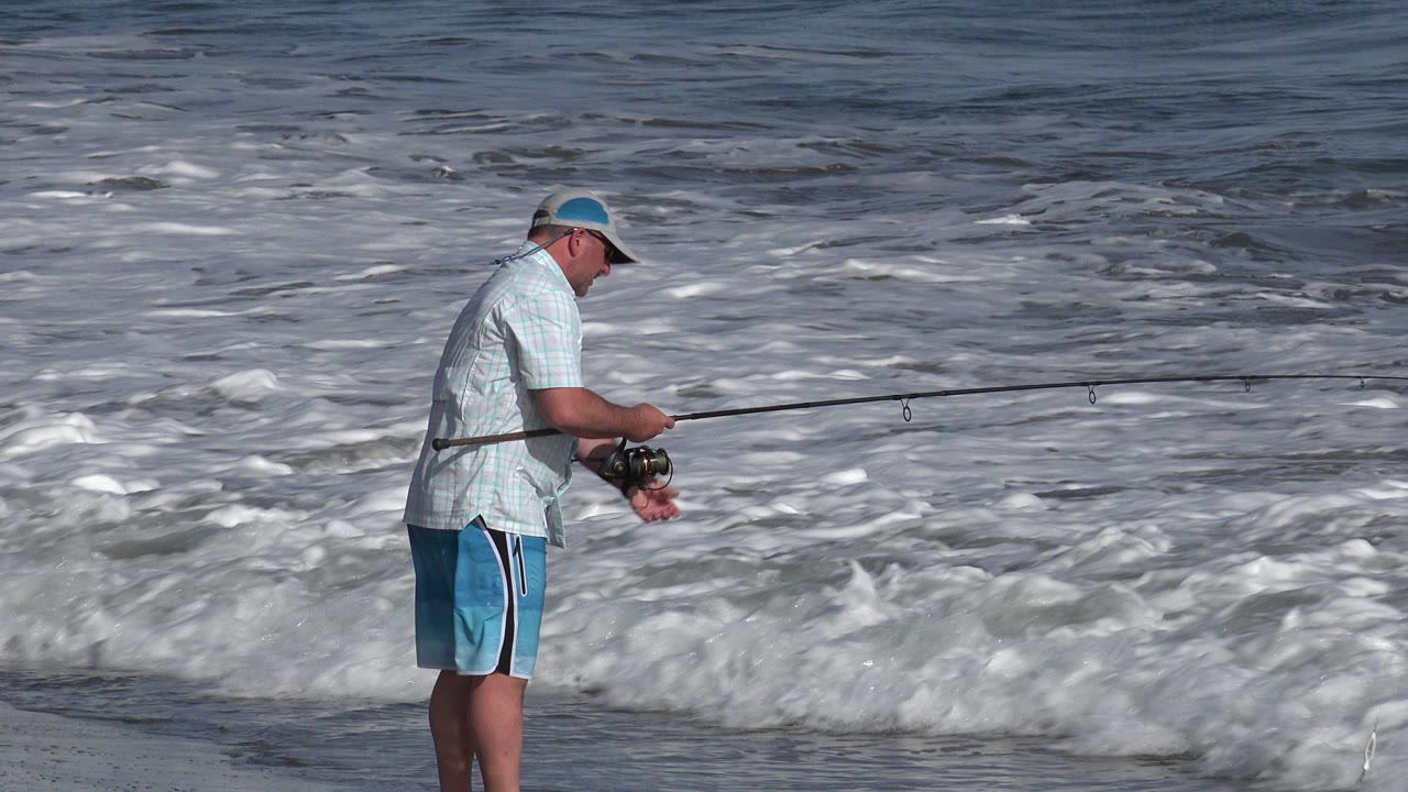 Fisherman standing at the surf with a long rod over breaking waves.