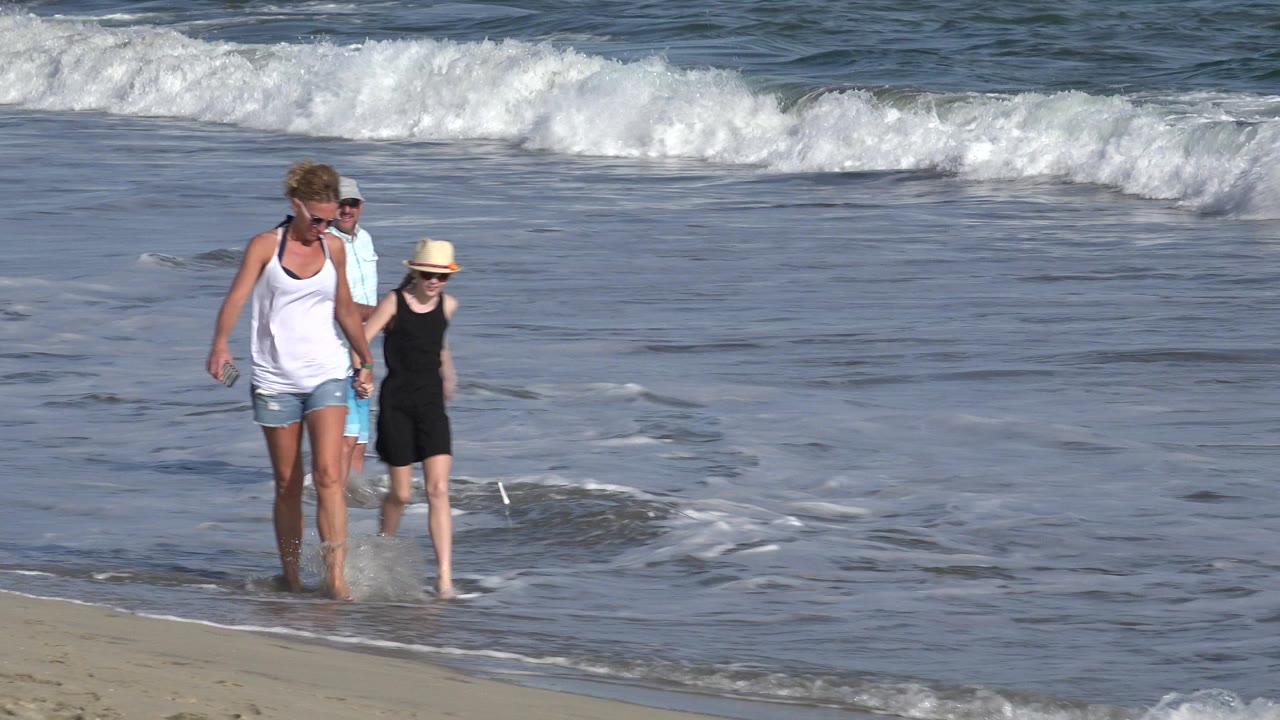 Woman and young girl walking barefoot at the edge of the surf.