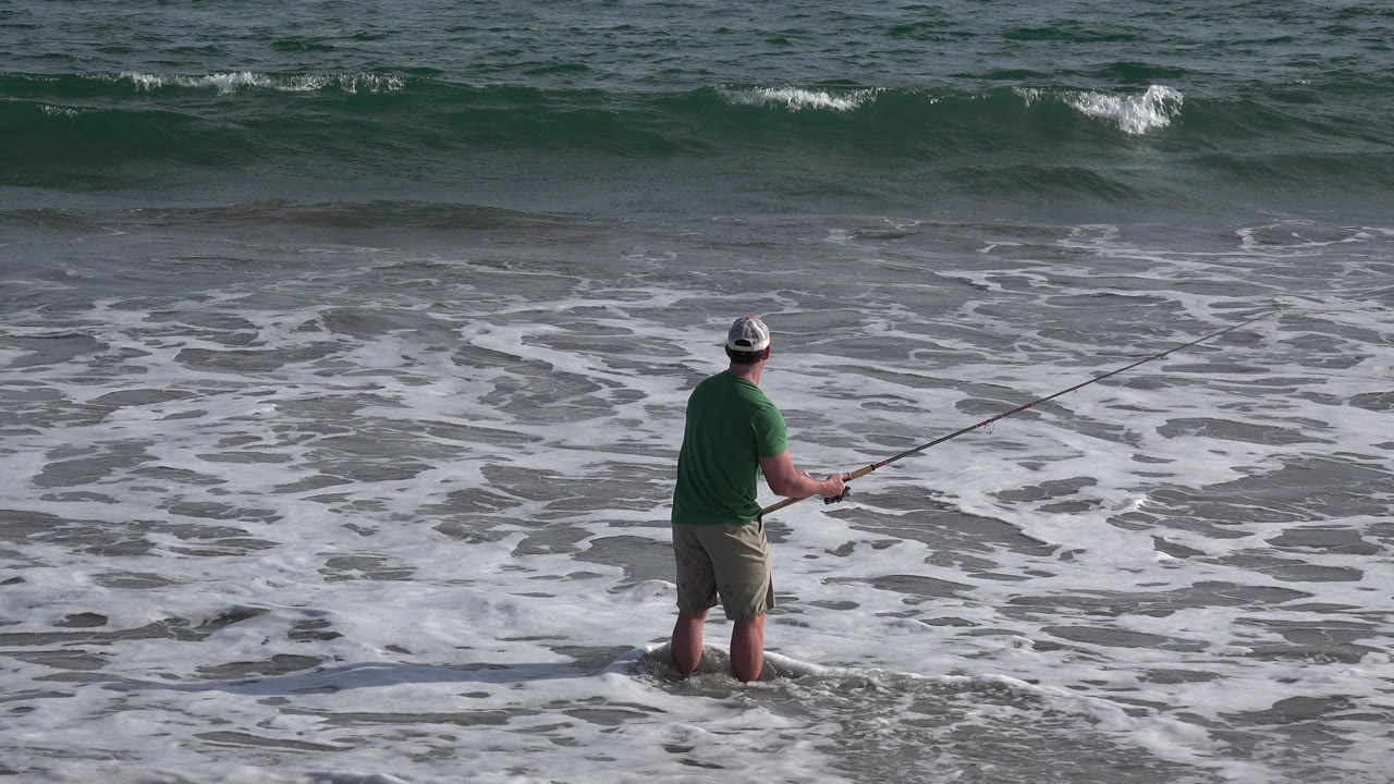 Man in green shirt fishing in shallow surf