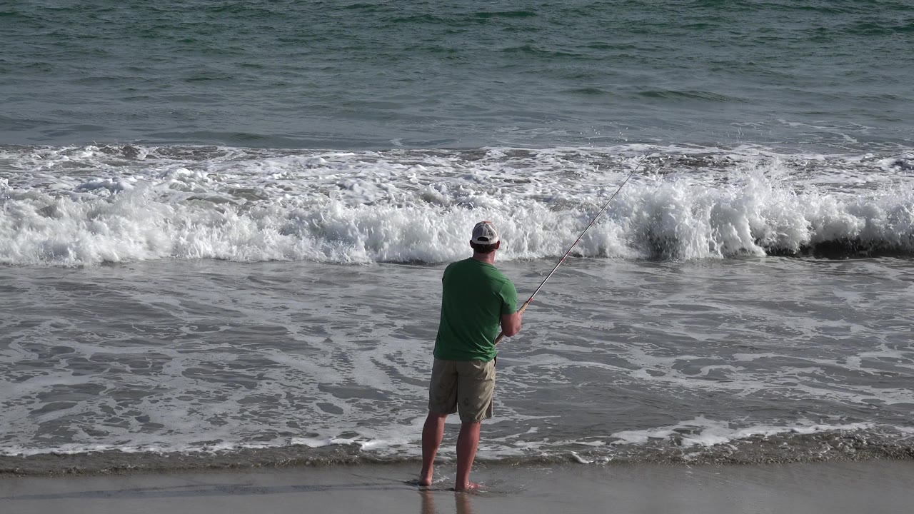 Man fishing as larger surf rises behind him