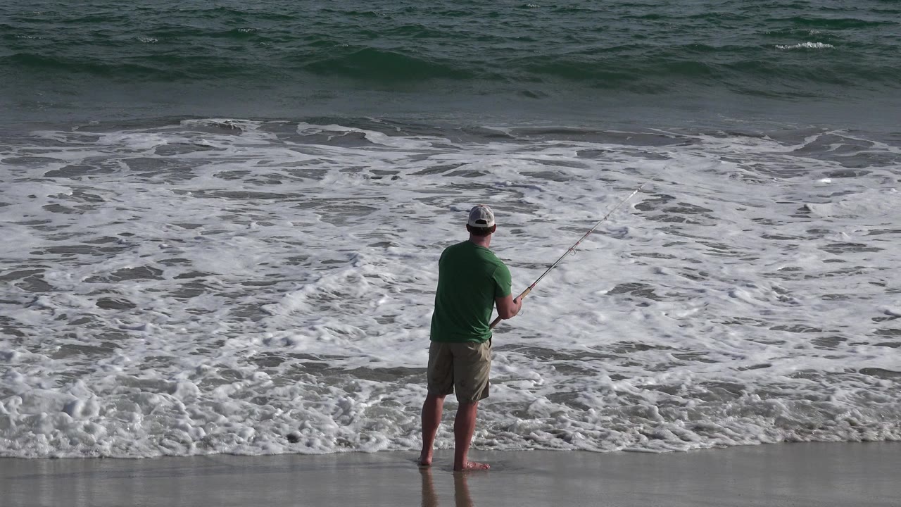 Man fishing at the edge of ocean surf.
