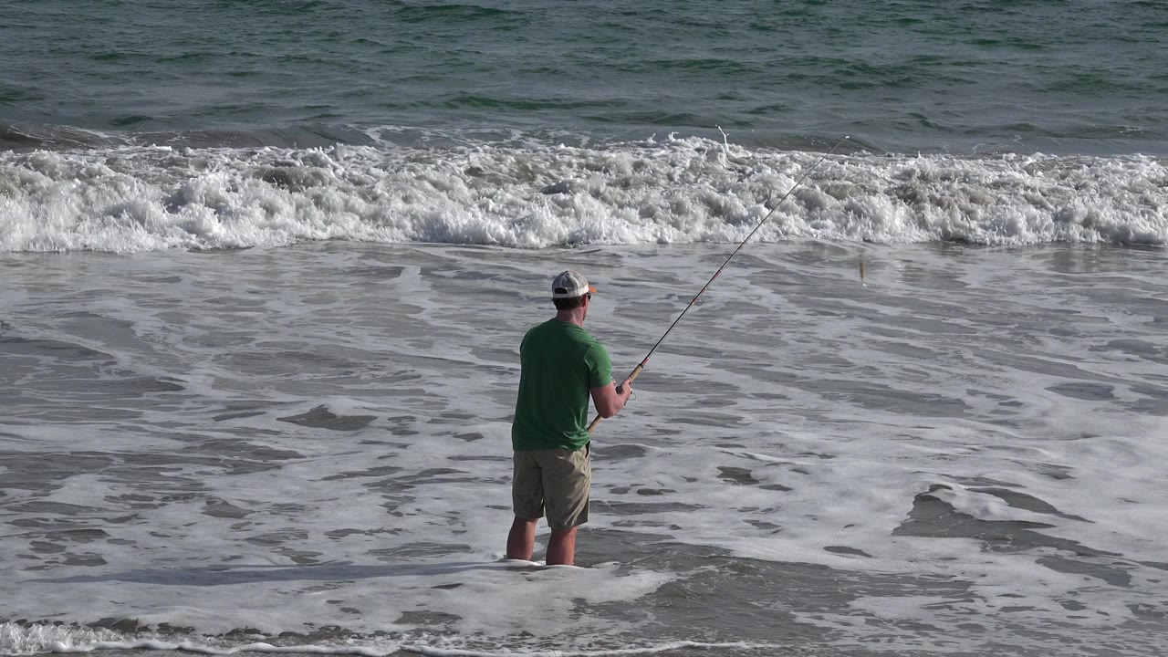 Man surf fishing at the edge of foamy ocean water.