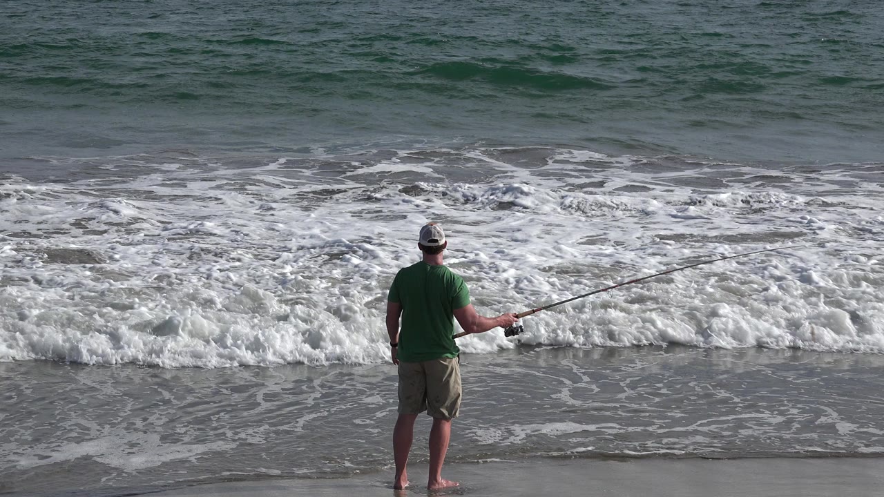 In Los Cabos, Mexico, the man remains centered on the wet sand with his fishing rod extended while whitewater spreads across the lower surf line.