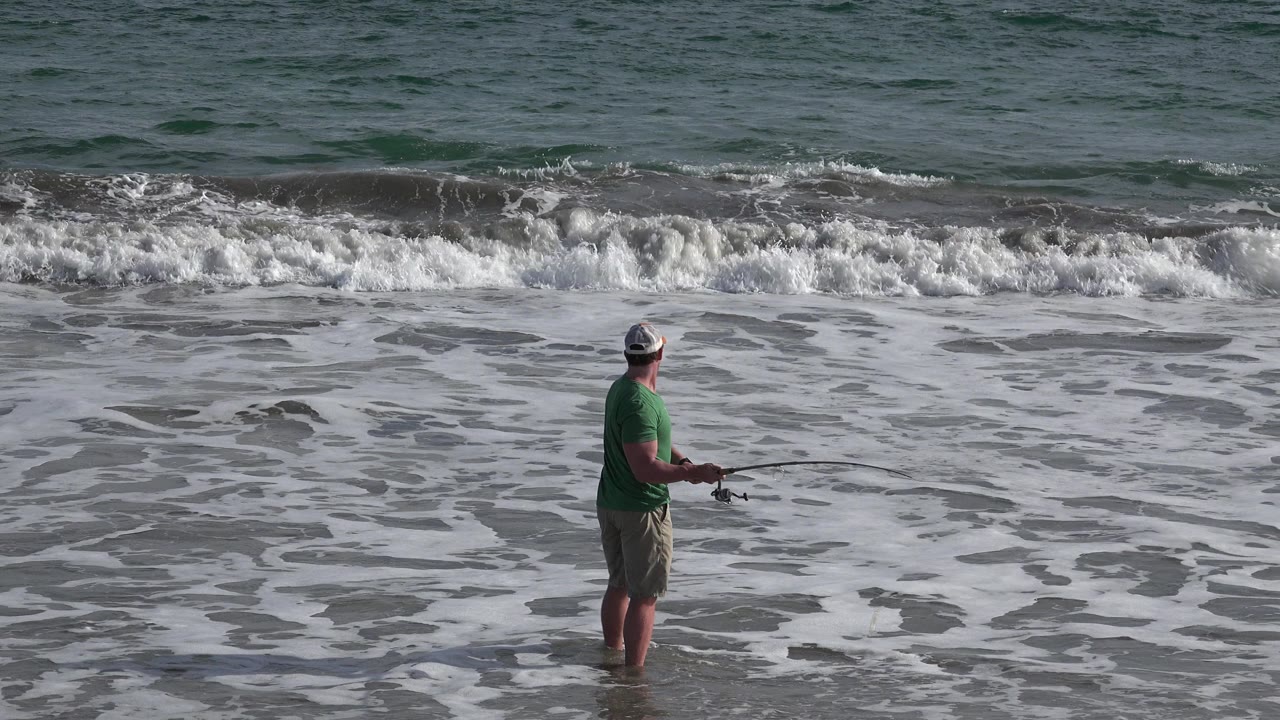 Man fishing in shallow surf on a beach.