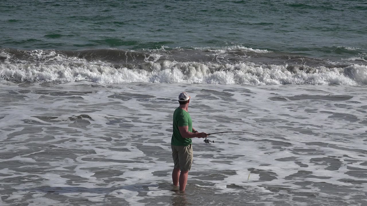 The fisherman remains centered in the lower frame in Los Cabos, holding the rod low while a band of white surf breaks behind him.