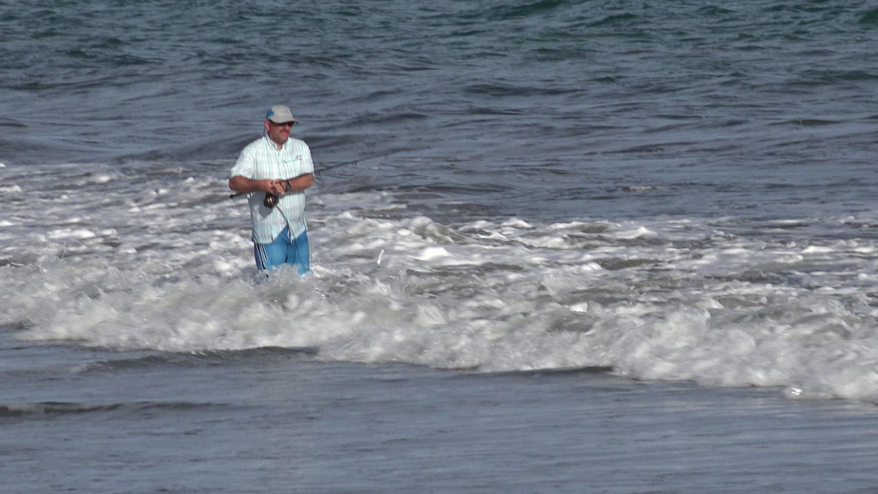 Man fishing in foamy surf near shore.