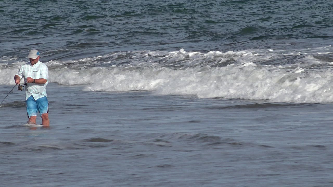 Man fishing knee-deep in surf at a beach.