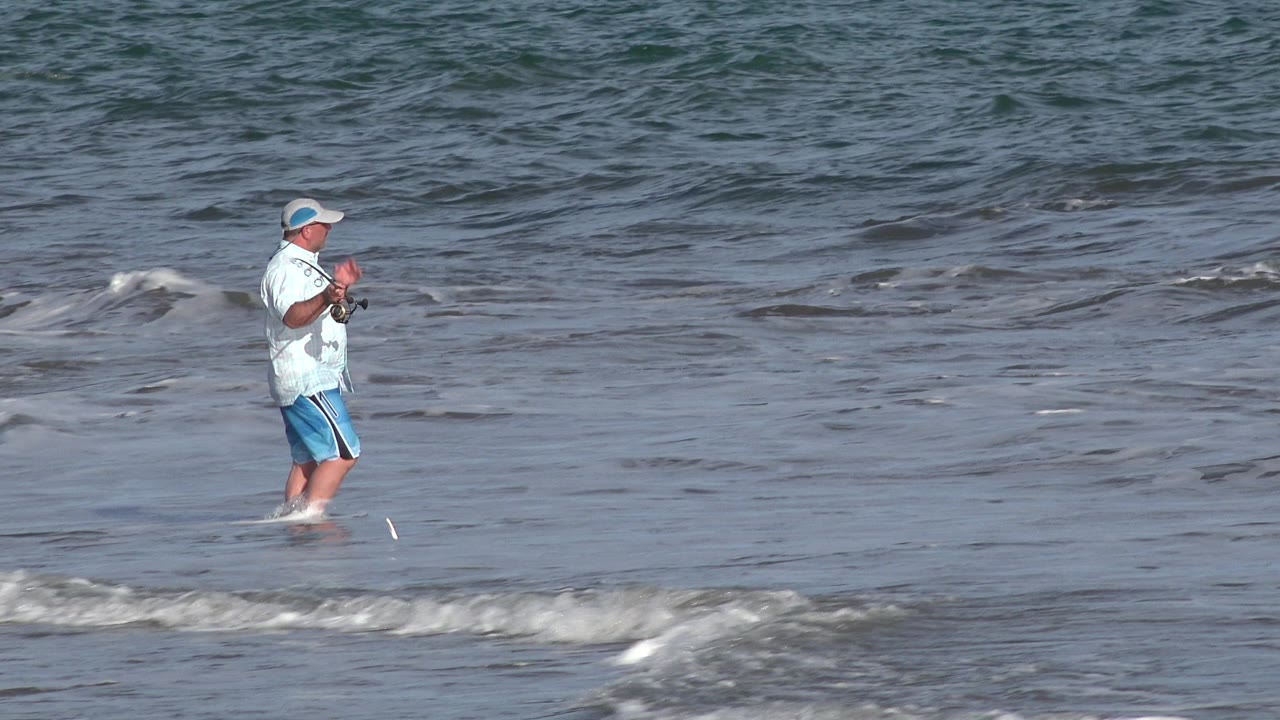 Man raises his fishing rod and reel in the surf.