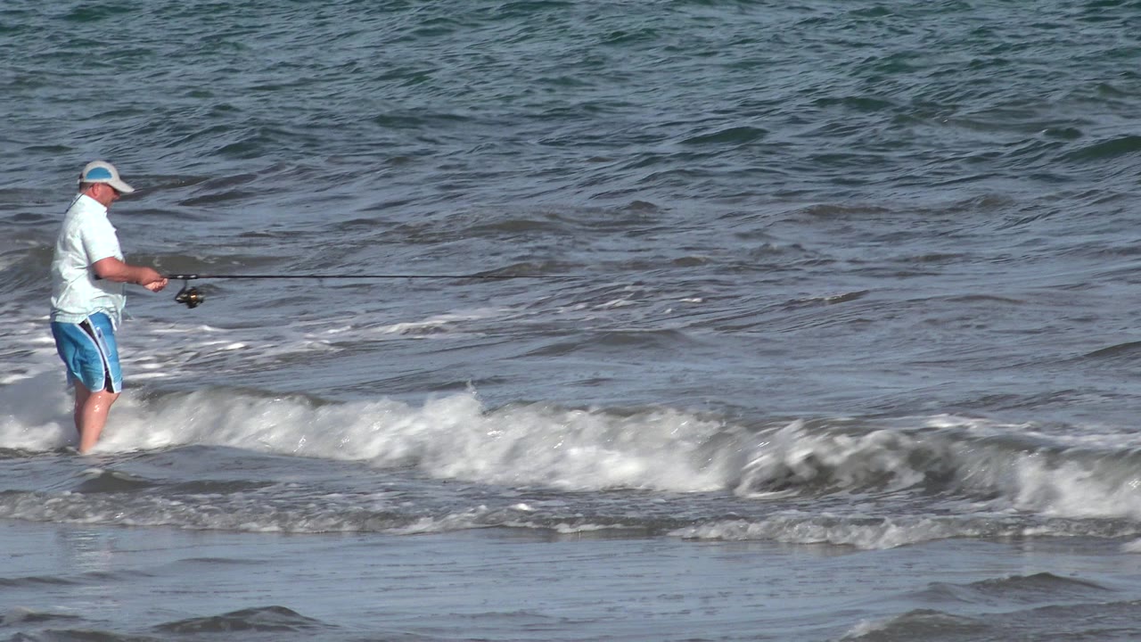 Adult man fishing in shallow ocean surf.
