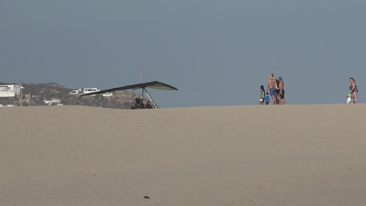 Wide sandy beach ridge with vacationers and a hang glider against blue sky.