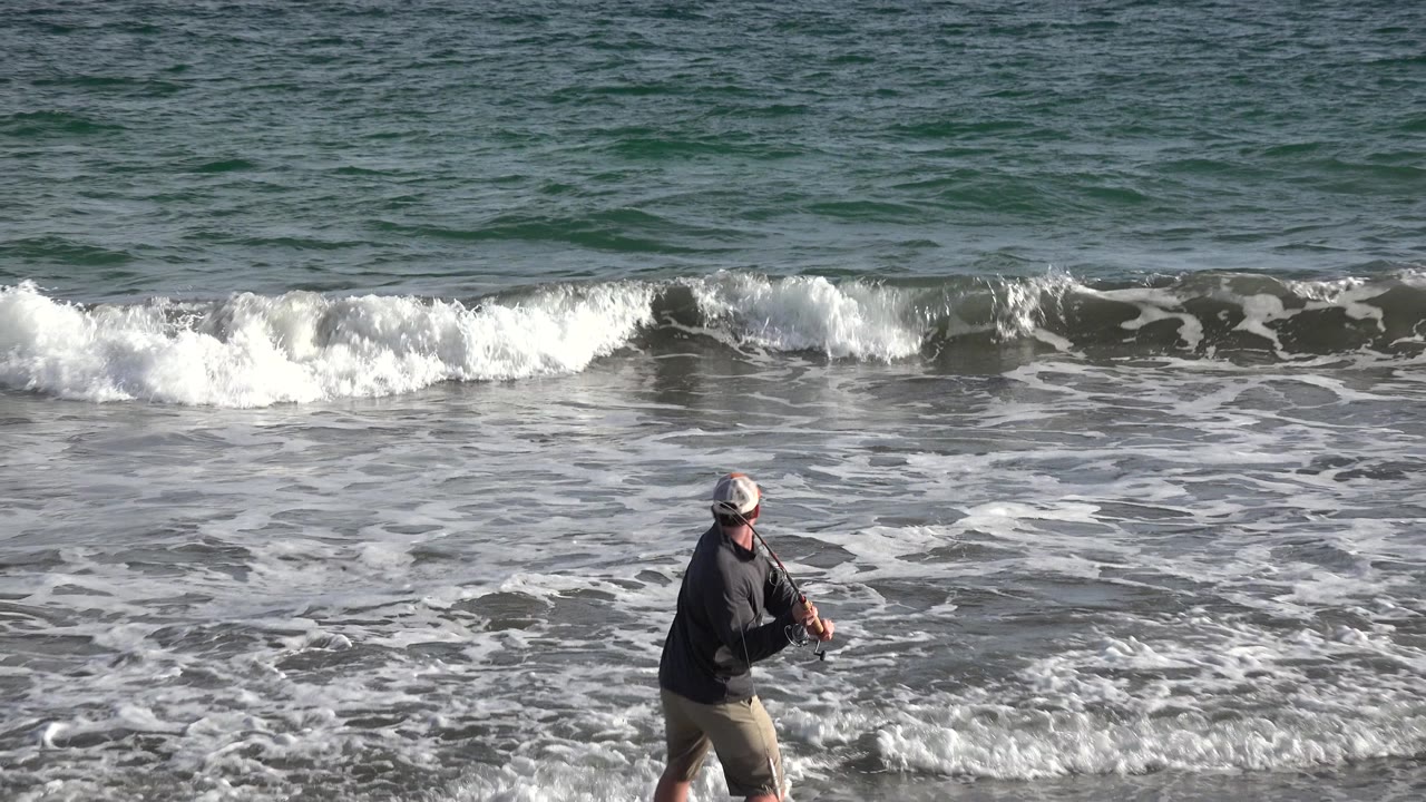 Man fishing at the edge of breaking surf.