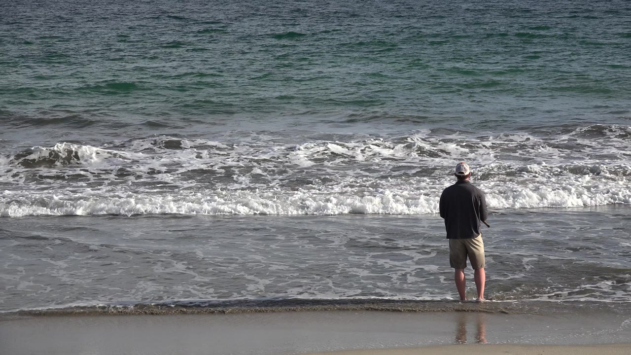 Fisherman seen farther right as waves spread across the shore.
