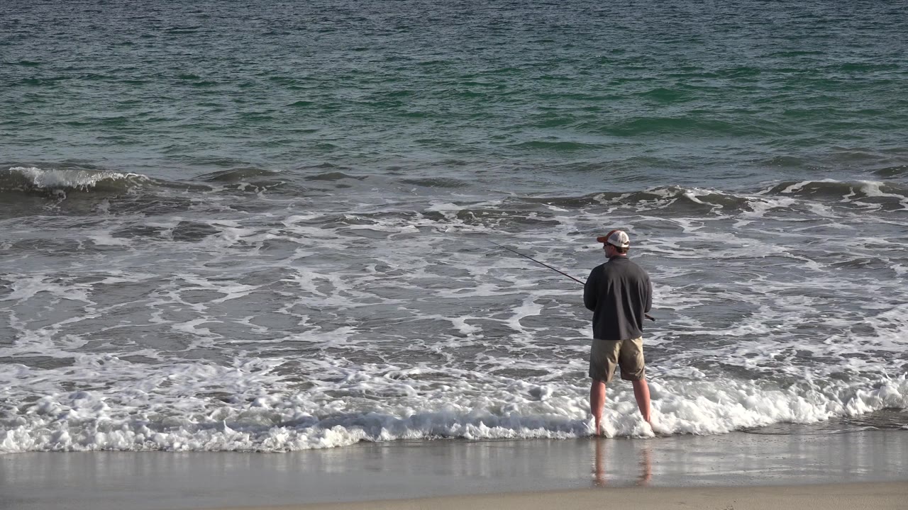 Adult standing near breaking waves on beach.