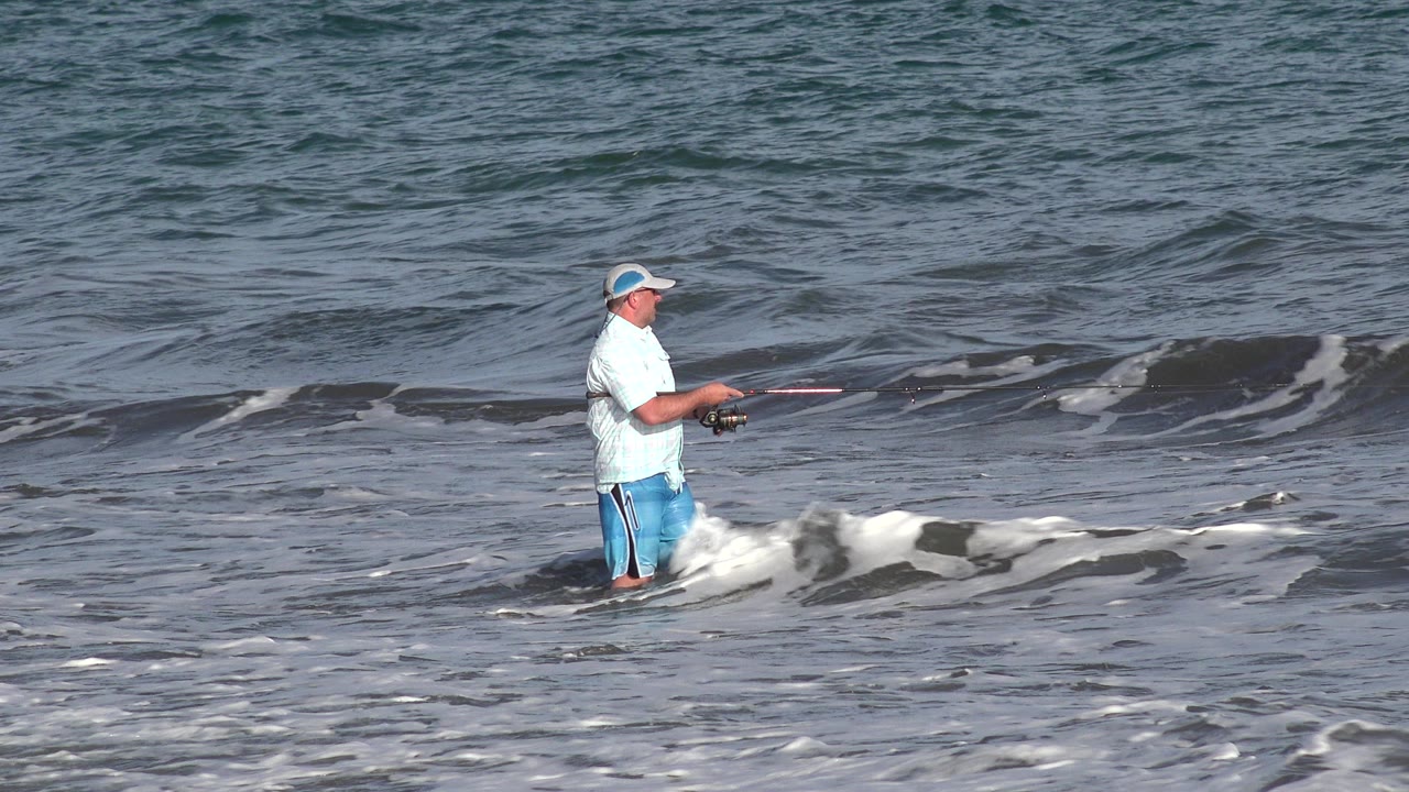 Man fishing in shallow ocean surf.