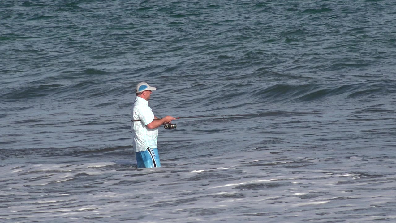 Man standing in ocean surf with a fishing rod.