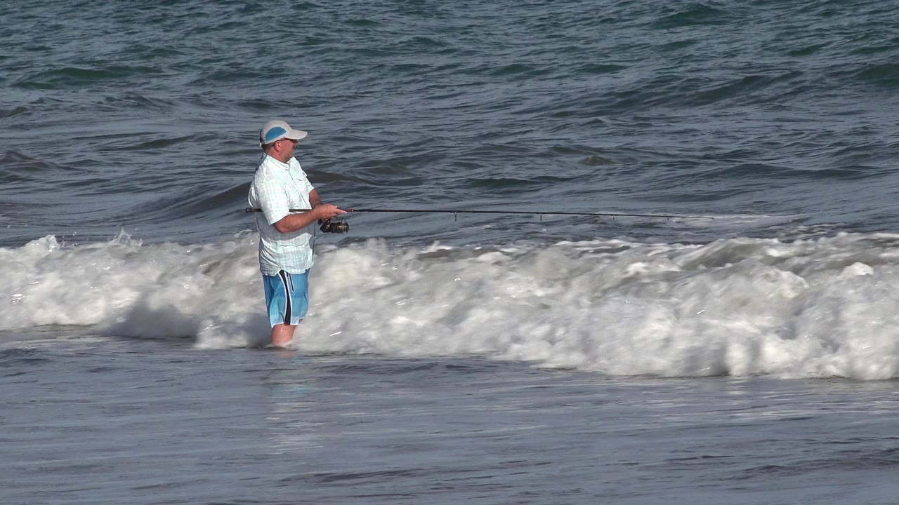 Adult fisherman standing in surf with a fishing rod.