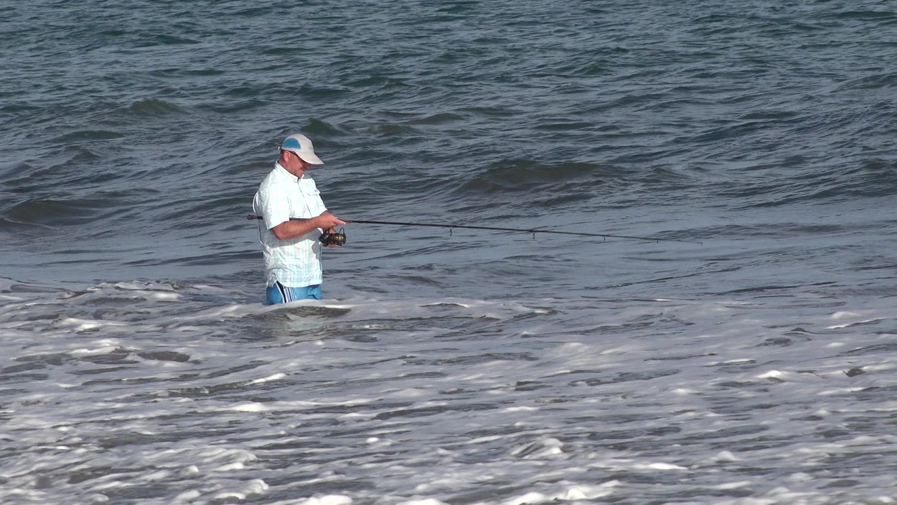Man fishing in shallow ocean surf.