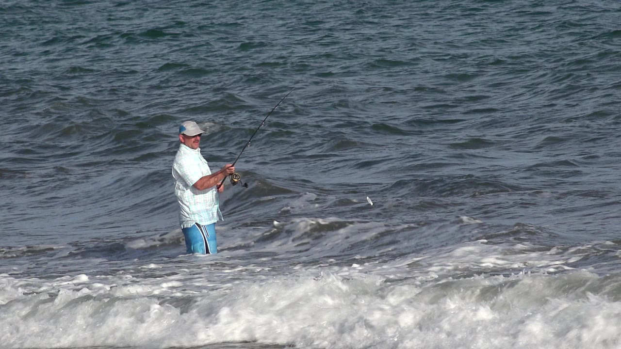 Man fishing waist-deep in ocean surf.