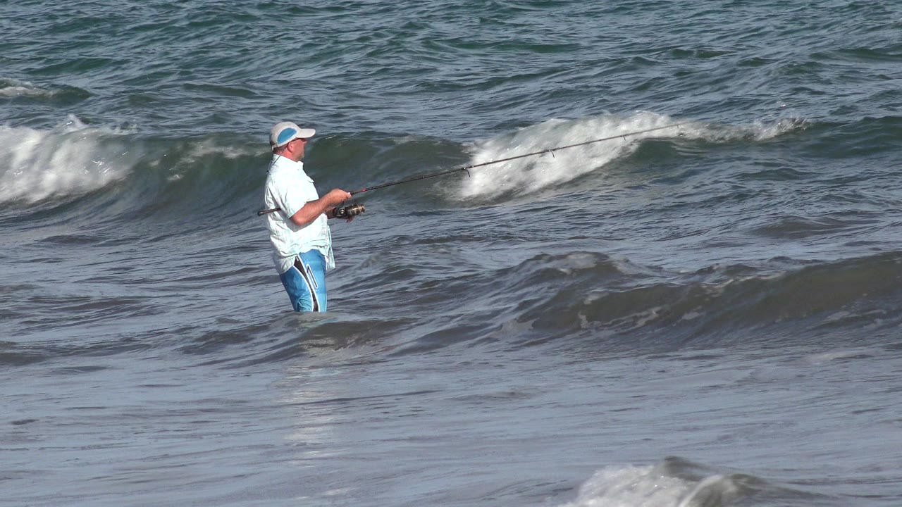 Angler standing in breaking ocean surf with a fishing rod.