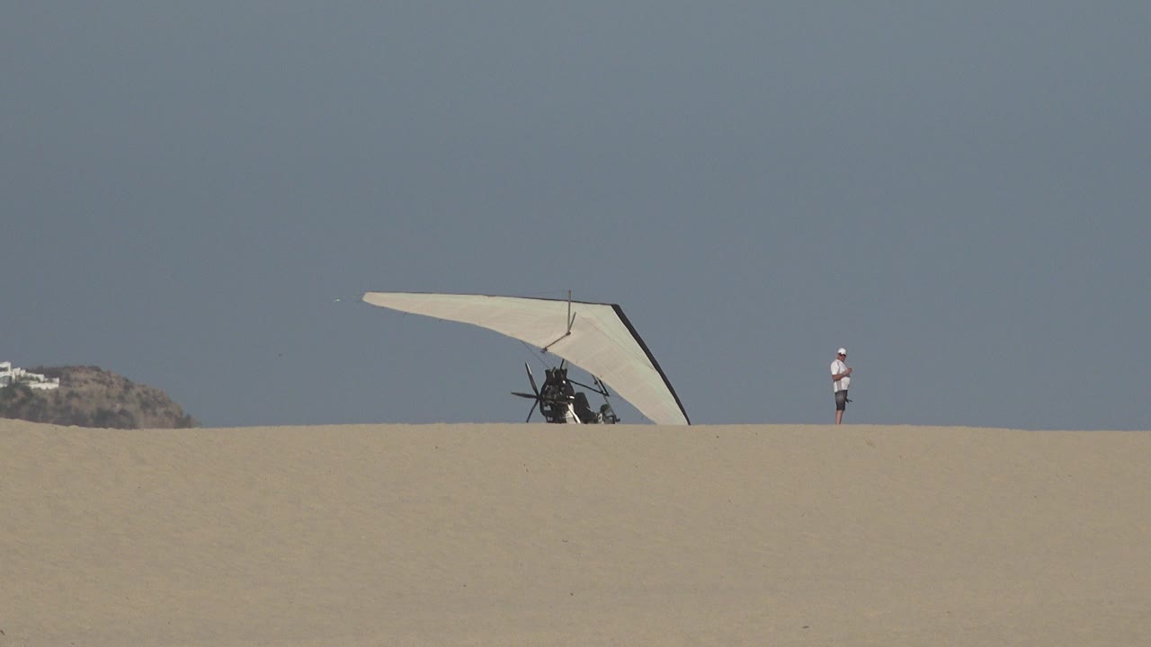 Man standing on sand near a hang glider under clear sky.