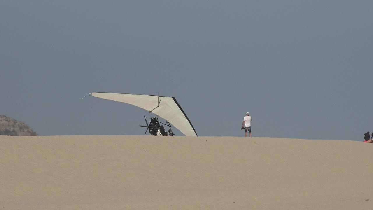 Hang glider and distant person on a sandy ridge under clear sky.