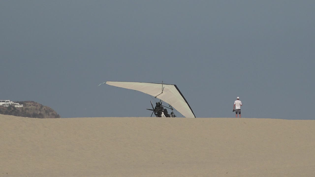 Winged sport device and person on a sandy dune under a clear sky.