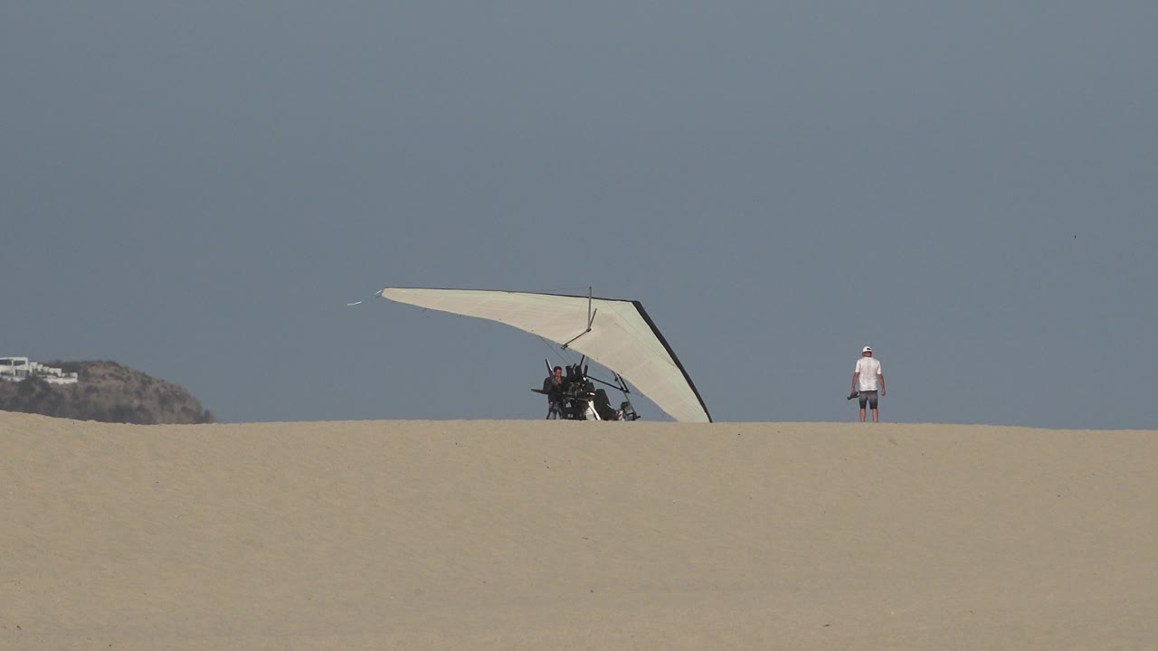 Hand glider low on the dune with a person standing to the right.