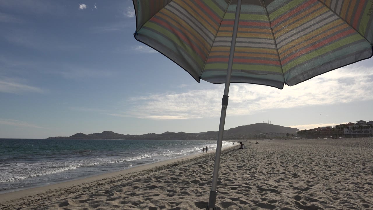 Beach umbrella above waves and sand.