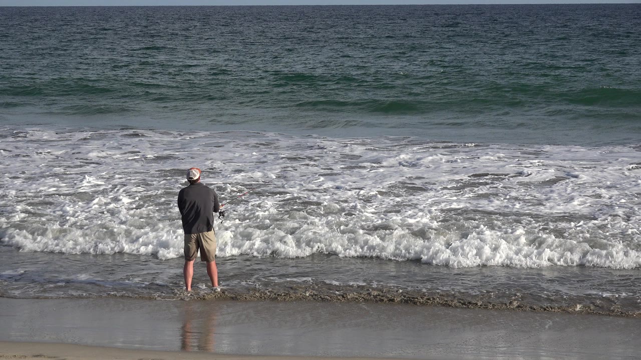Man standing at the shoreline as waves break in front of him.