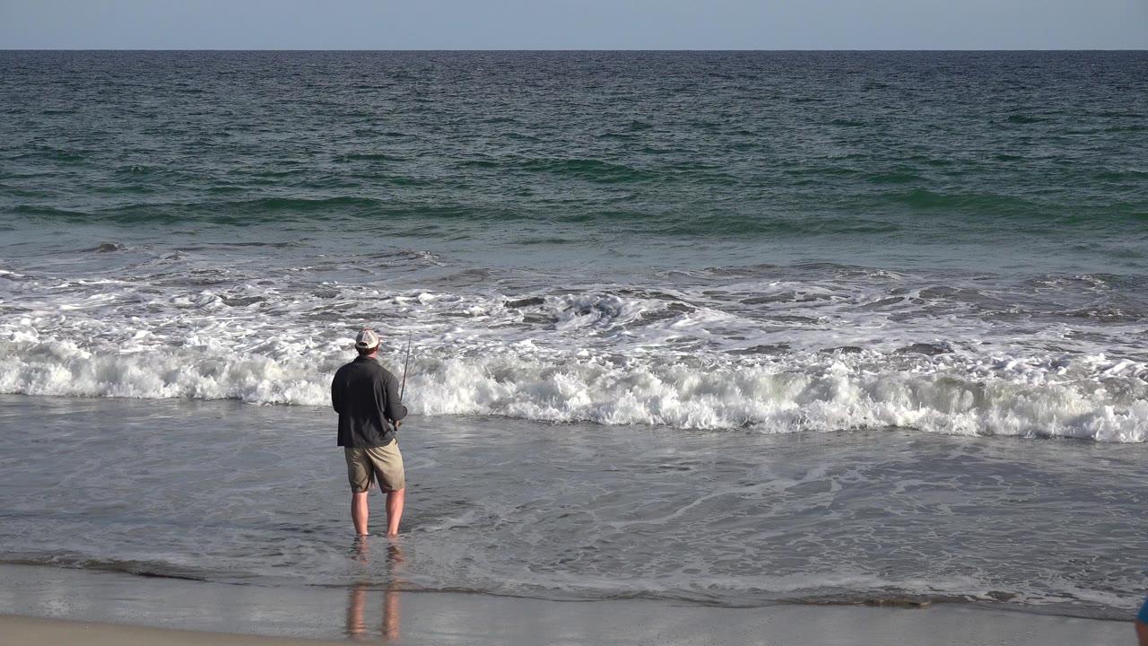 Man fishing at the shoreline with ocean waves ahead.