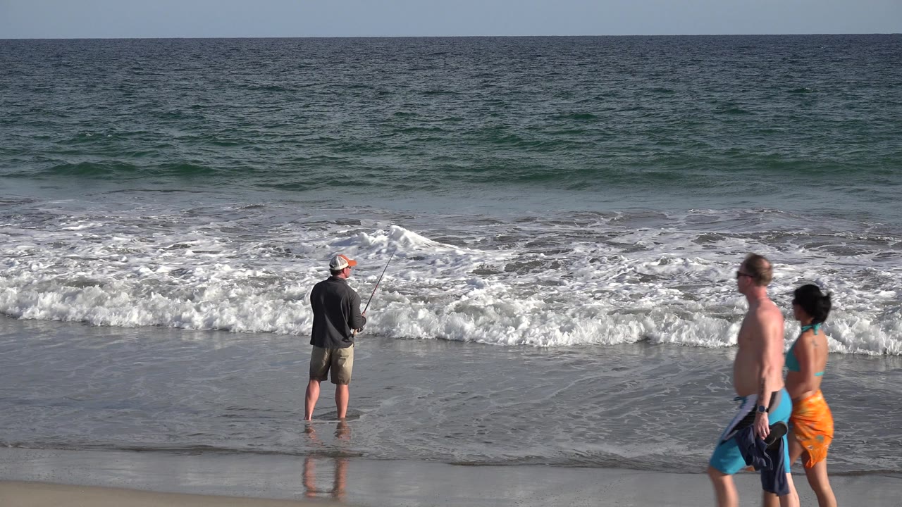 Fisherman at surf with a couple entering from the right.