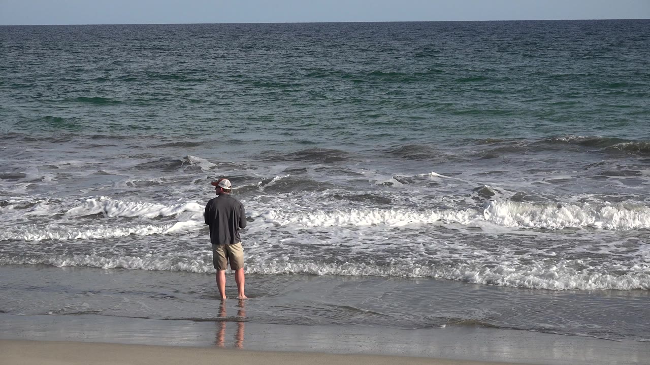 Man with fly rod watches a wave roll in.