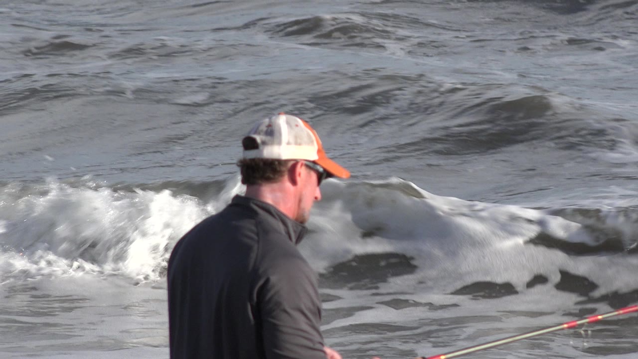 Man in cap fishing beside small ocean waves.